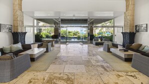 Eine großzügige Lobby mit modernem Design, ausgestattet mit einer gemütlichen Sitzecke mit Sofas und Sesseln, einem zentralen Couchtisch und Blick ins Freie durch große Glaswände.