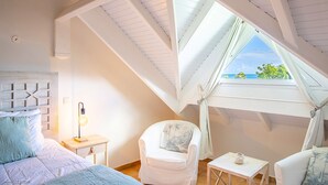 Ein Schlafzimmer mit Dachfenster, einem Bett, einem Sessel, einem Nachttisch und einem kleinen Tisch.