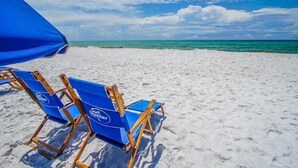 A beach with two blue lounge chairs and a blue umbrella.