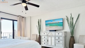A hotel room with a bed, a ceiling fan, a TV displaying 'Legacy Vacations', and two large vases.
