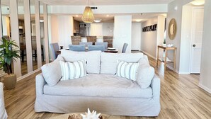 A living room with a grey sofa, a hanging light fixture, and a dining area in the background.