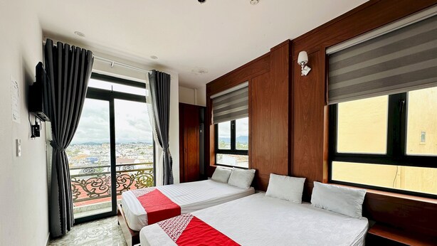 A hotel room with two beds, a balcony with a view, and a large window with blinds. - OYO 1204 Hoang Linh Hotel (Xuan Huong - Da Lat)