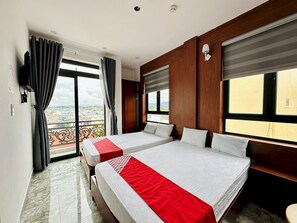 Una camera d'albergo con due letti, un balcone e una grande finestra con tende.