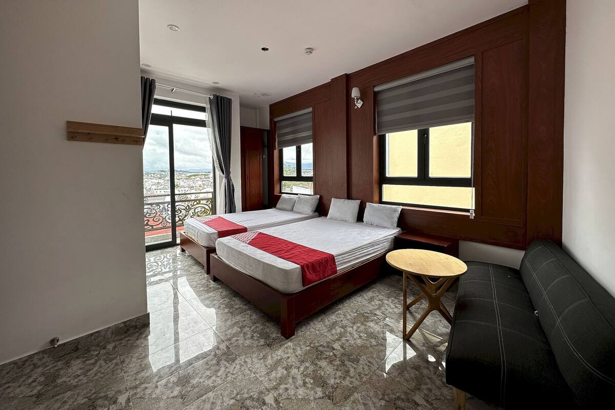 A hotel room with two beds, a sofa, a small table, and a balcony with a view.