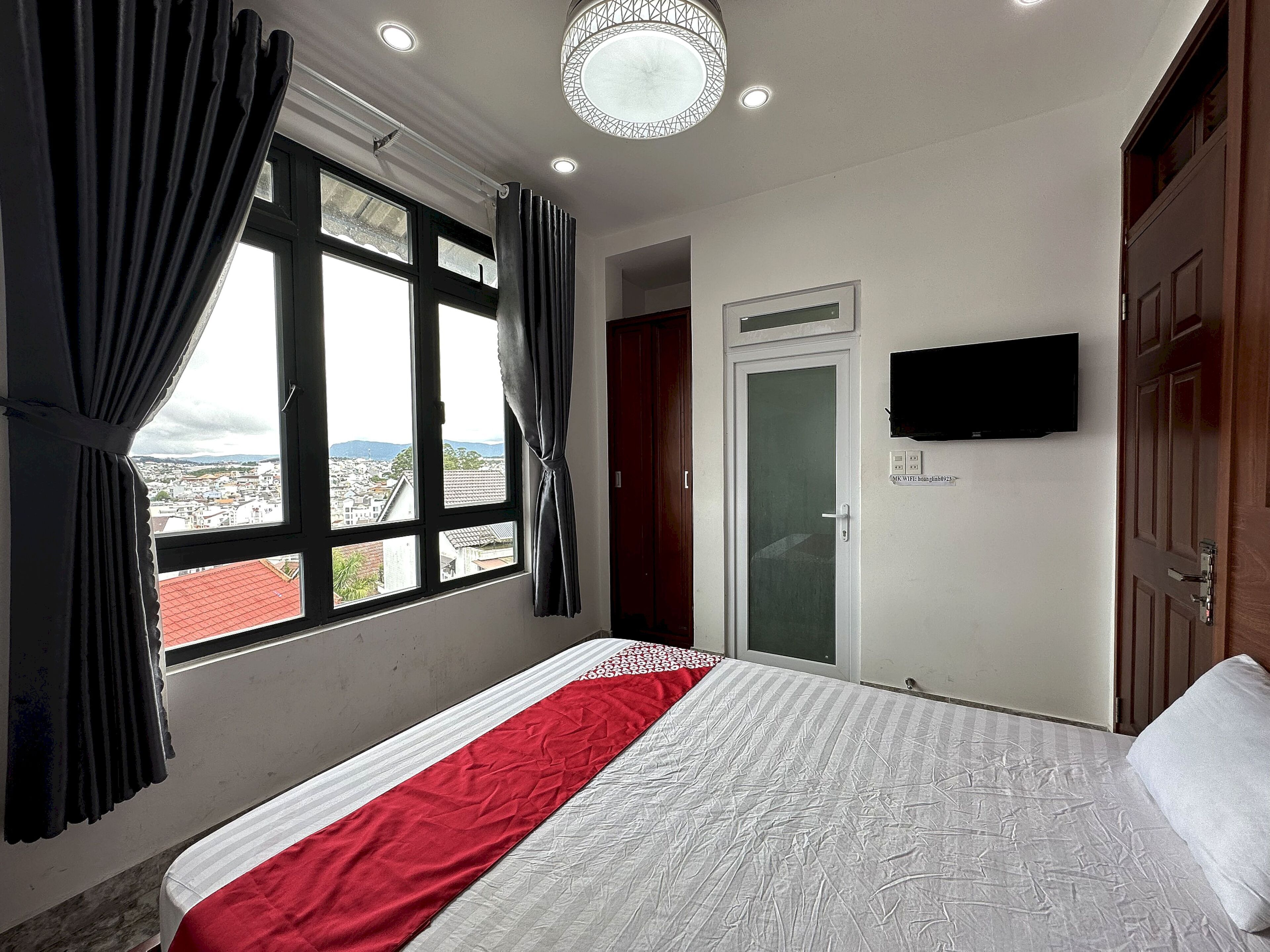 Habitación de hotel con cama, televisión en la pared y ventana con cortinas.