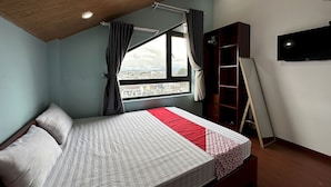 A bedroom with a bed, a window with curtains, a bookshelf, and a TV on the wall. - OYO 1204 Hoang Linh Hotel (Xuan Huong - Da Lat)