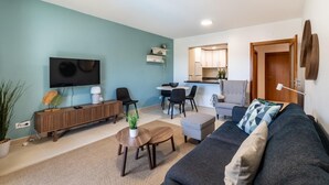 Una sala de estar moderna con sofá, mesa de centro y televisor. Se observa un comedor con sillas y una cocina al fondo.