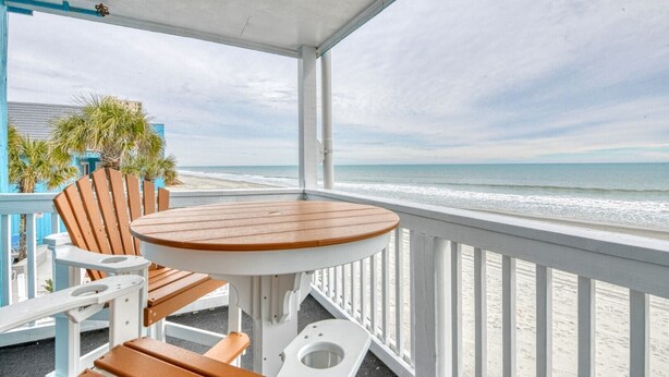A balcony with a wooden table and chairs, overlooking a beach. - Beach House 217, two-bedroom, two-bath ocean front condo (Garden City Beach)