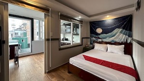 Quarto de hotel com cama, um espelho grande, uma tapeçaria com céu noturno e vista da cidade através de uma porta deslizante.