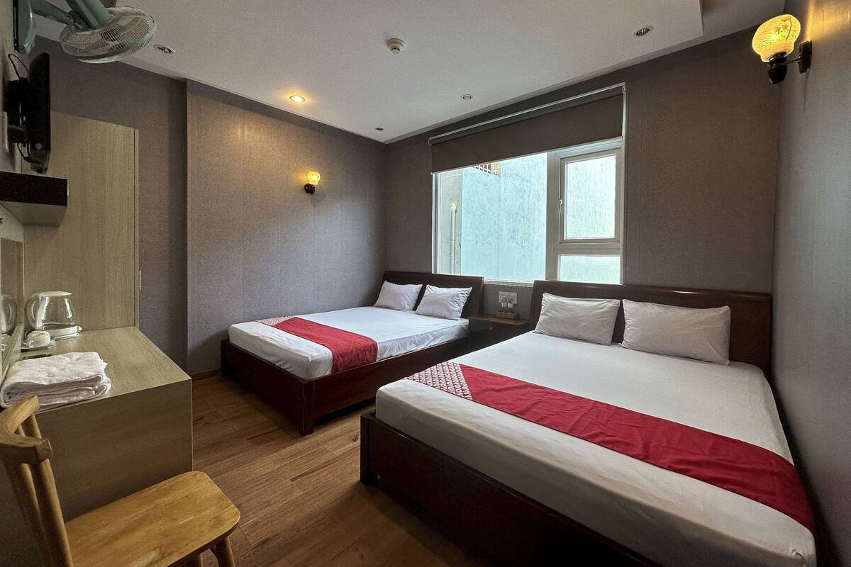 A hotel room with two beds, a desk, and a window.