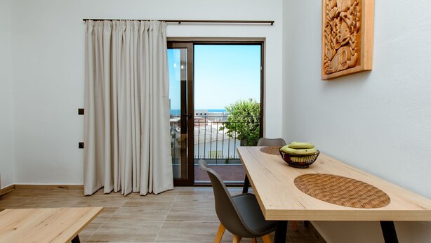 A modern room with a wooden table, black chairs, a view through a glass door, and a wooden carving on the wall. - Krinis houses next the old harbour (Chania)