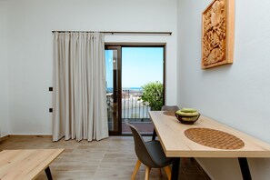 Una habitación moderna con una mesa de madera, sillas negras, vistas a través de una puerta de cristal y una talla de madera en la pared.