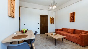 A modern living room with a wooden dining table, blue chairs, a red sofa, and a small coffee table. - Krinis houses next the old harbour (Chania)