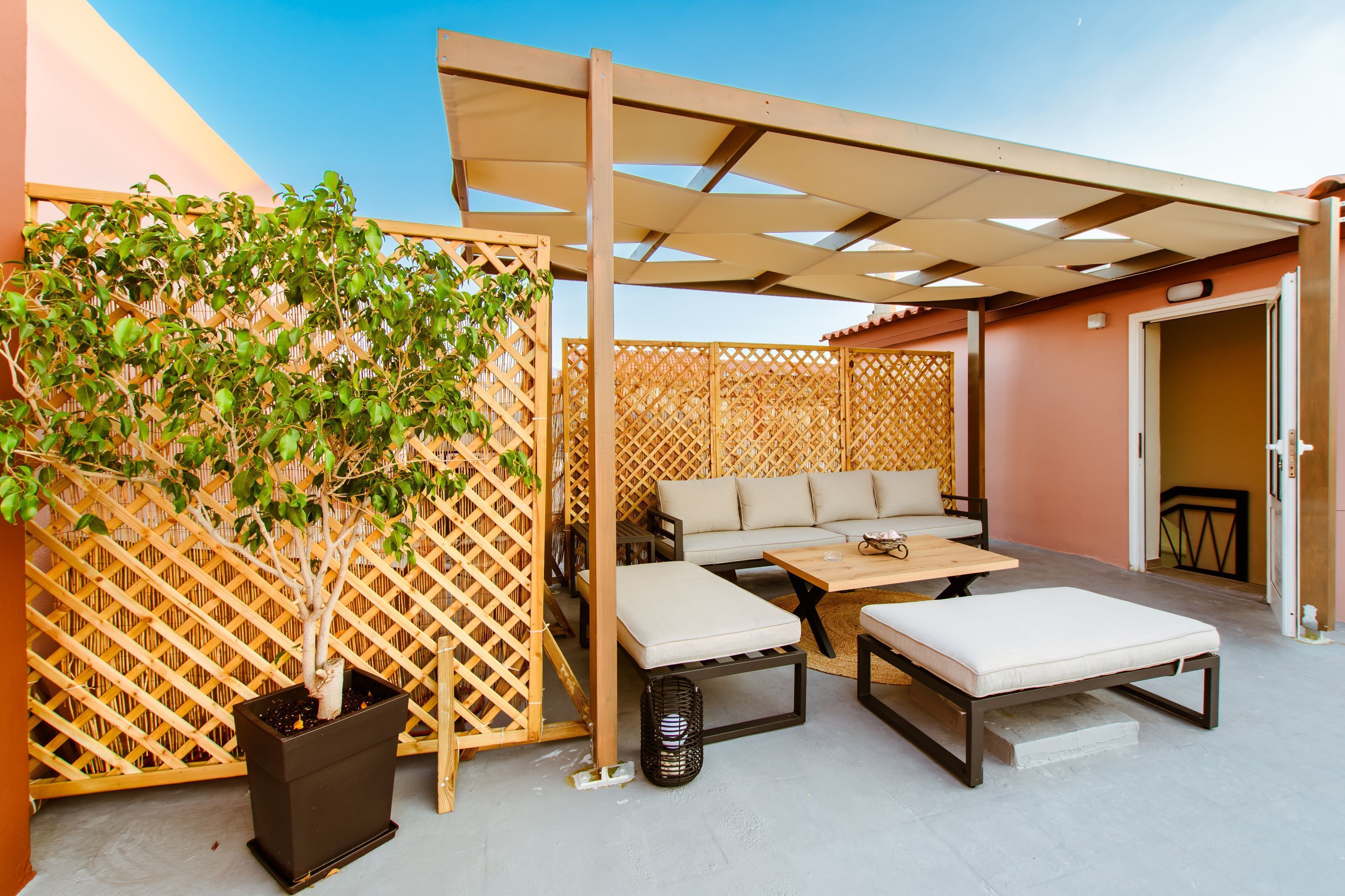 Un espace extérieur aménagé en patio, avec une clôture en treillis de bois, un arbre en pot, un canapé et une table.