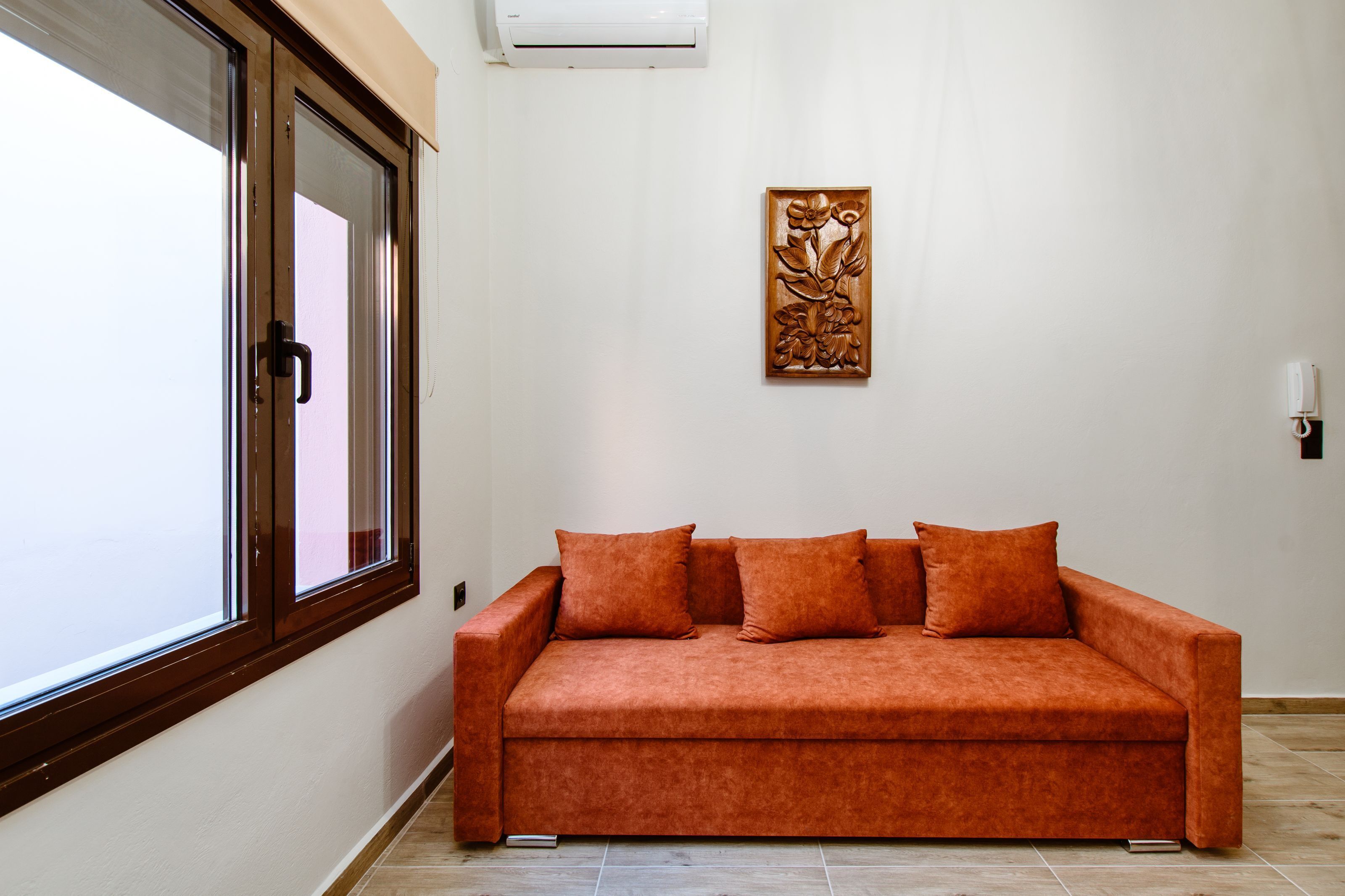 A room with a sofa, a window, and a wall-mounted artwork.