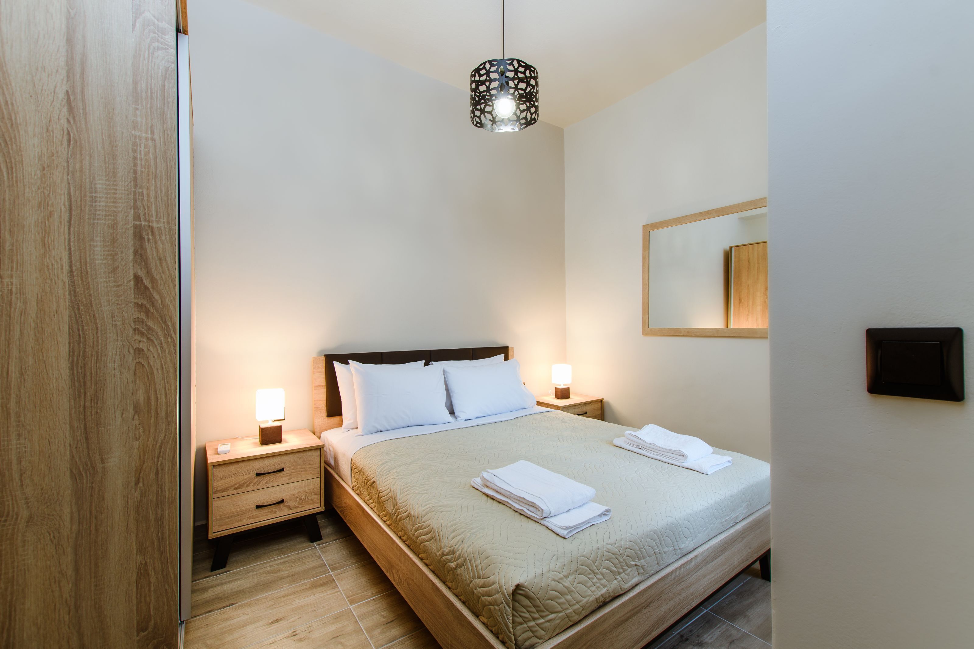 A neatly made bed with white linens, a bedside table with a lamp, and a hanging light fixture.
