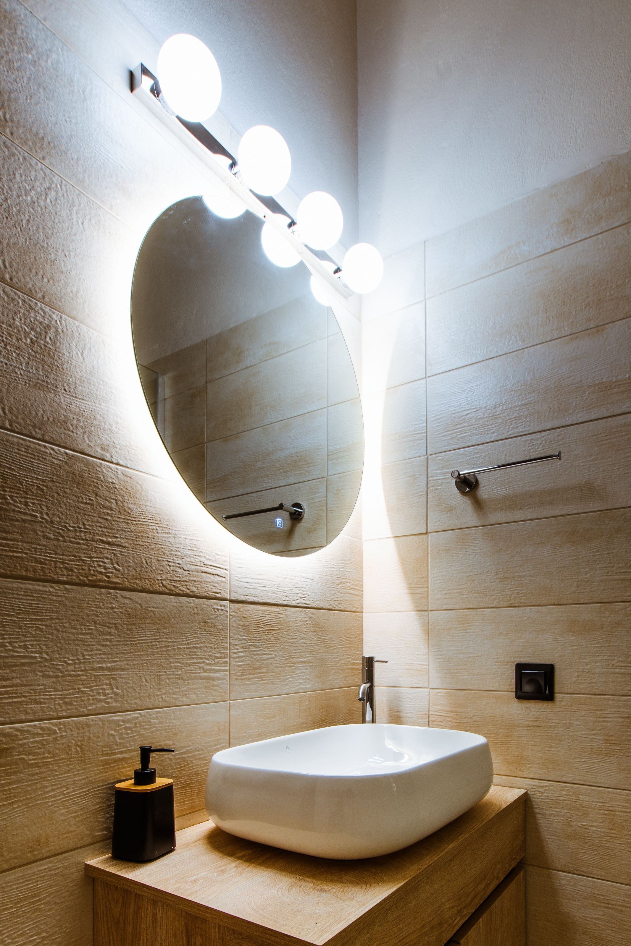 Un baño con un espejo ovalado grande, un lavabo blanco y un dispensador de jabón.