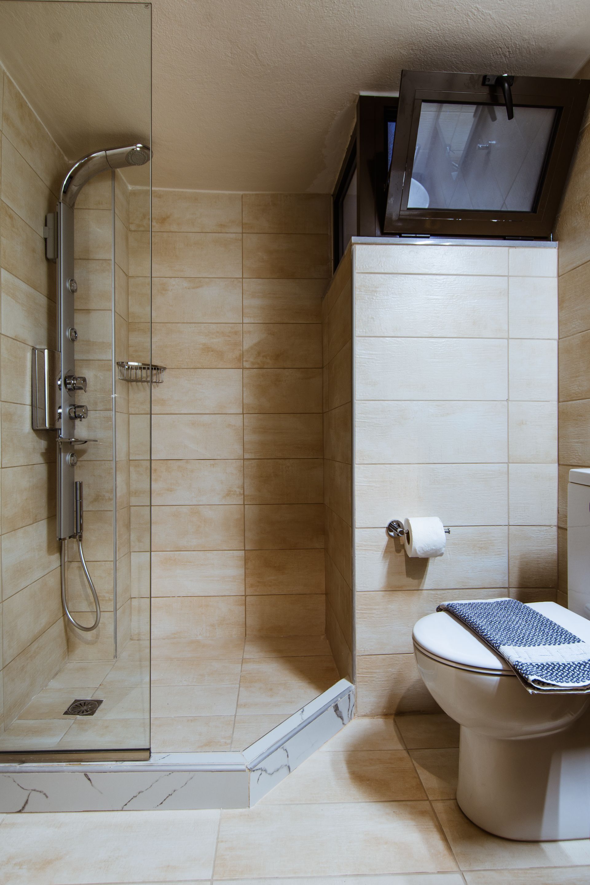 A bathroom with a shower, toilet, and a window above the toilet.