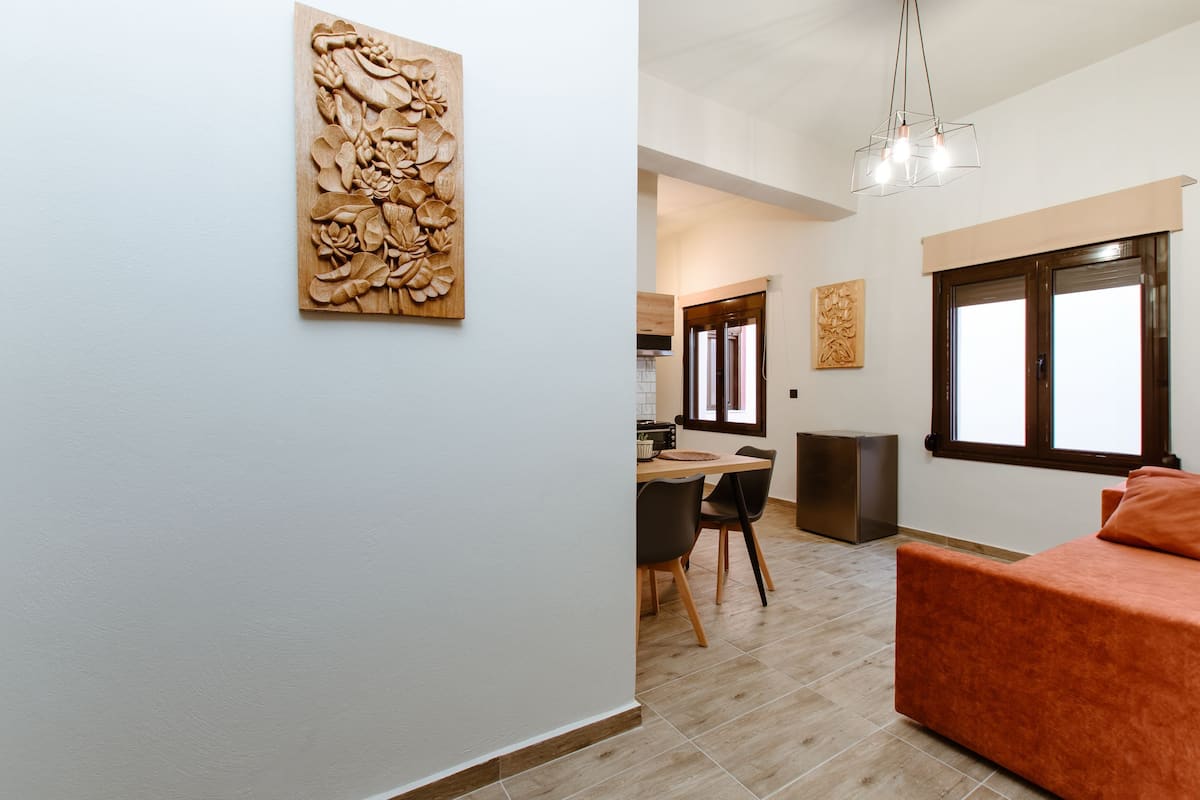 A modern living room with a sofa, dining area with chairs, and a kitchen in the background.