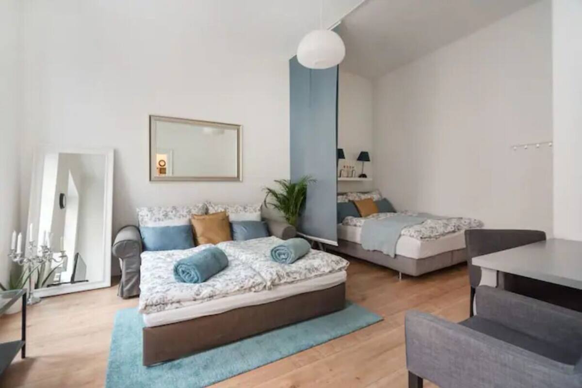A modern bedroom with a large bed, a smaller bed, a desk, and a mirror.