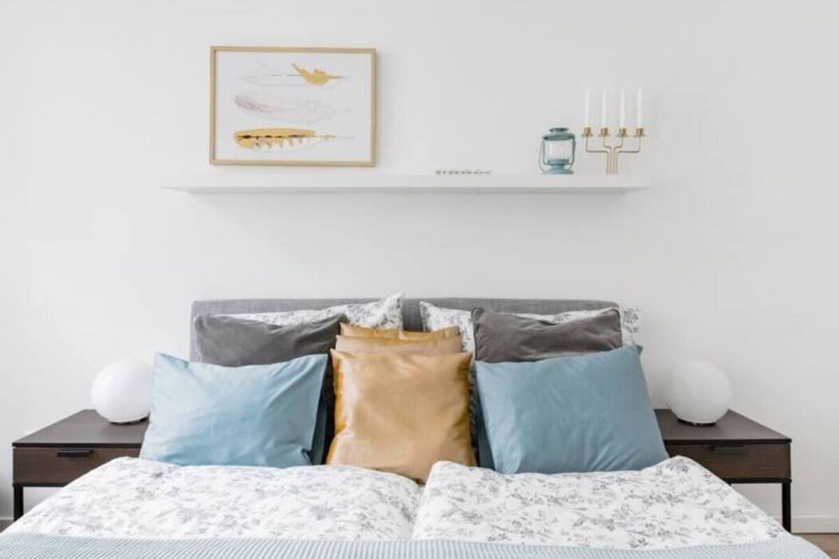 A neatly made bed with patterned bedding, a framed artwork above it, and a menorah on a shelf.