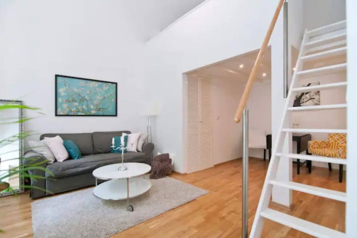 A modern living room with a grey sofa, a round coffee table, and a staircase with a white railing.