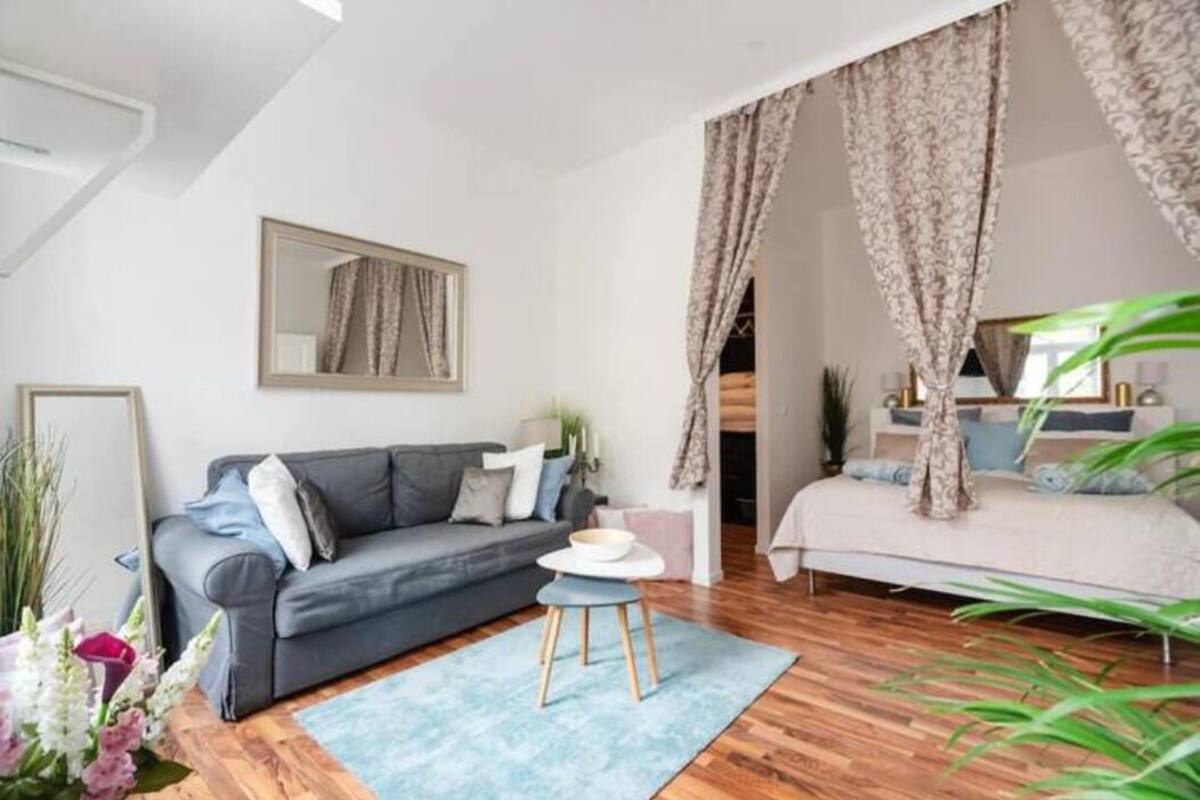 A modern bedroom with a grey sofa, a bed with a canopy, a small round table, and a mirror on the wall.