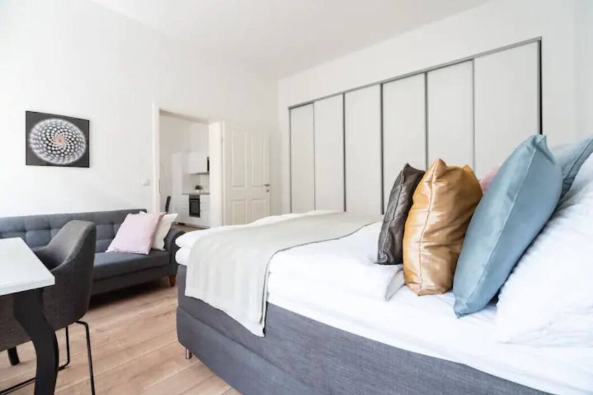 A modern bedroom with a large bed, a grey sofa, and a dining table.