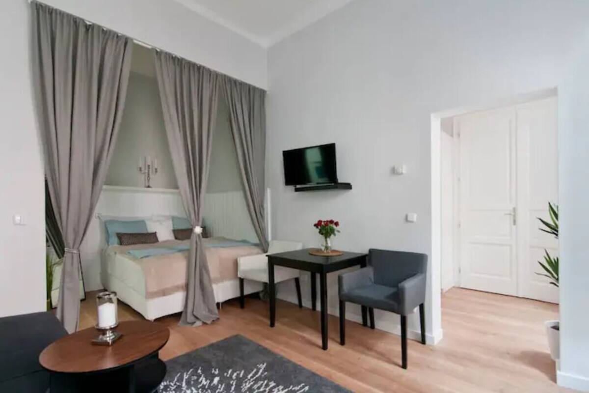 A modern bedroom with a bed, a TV, a small table with a vase, and a chair.