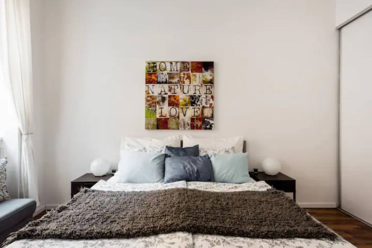 A bedroom with a bed, pillows, a blanket, and a wall art piece.