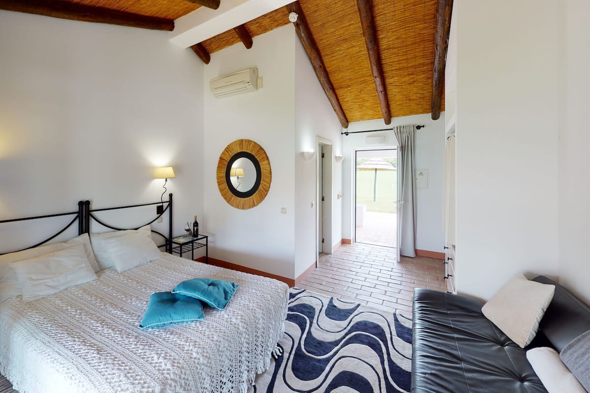 A bedroom with a bed, bedside tables, a lamp, a mirror, and a view of the outside.