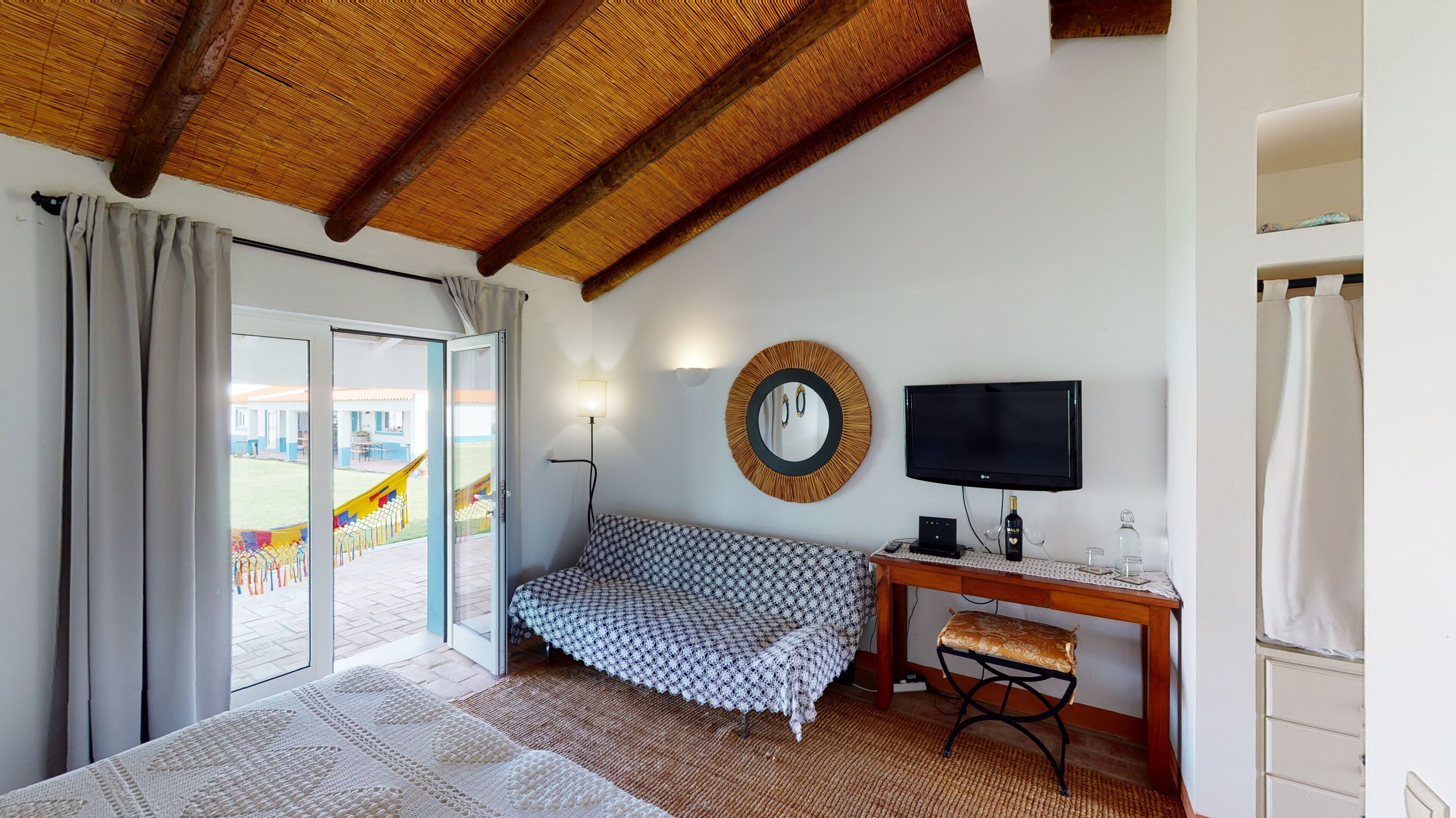 Un dormitorio con cama, escritorio, silla, televisor y ventana con cortinas.