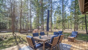 Ulkoterassi, jossa on puinen pöytä ja siniset tuolit, ja jonka ympärillä on metsäinen alue.