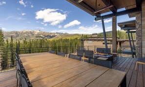 Terraza de madera con mobiliario exterior y una chimenea, con vistas a un paisaje montañoso.