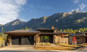Una casa moderna con garaje, un patio cubierto y montañas al fondo.