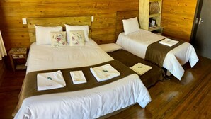 Una habitación tipo cabaña de madera con dos camas, cada una con sábanas blancas y almohadones florales. Tiene pisos de madera y cabecera de madera.