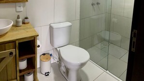 Un baño con inodoro, cabina de ducha de vidrio, tocador de madera con lavabo y espejo.