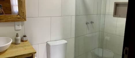 Een badkamer met toilet, douchecabine van glas, houten wastafelmeubel met wastafel en een spiegel.
