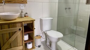 Un baño con tocador de madera, lavamanos blanco, inodoro y cabina de ducha con mampara de vidrio.