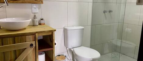 Een badkamer met een houten wastafelmeubel, een witte wastafel, een toilet en een douchecabine van glas.