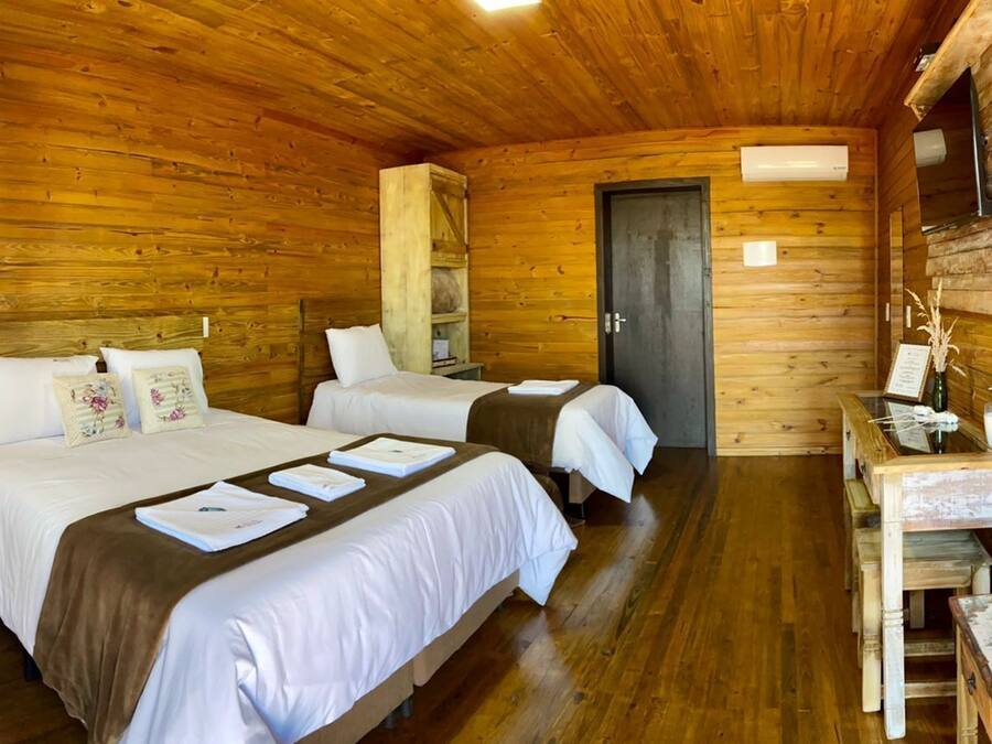 A wooden cabin room with two beds, a small table, and a shelf.