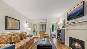 A living room with a sofa, ottoman, fireplace, television, and a map on the wall. - GC106•walk downtown•onsite pool•private hot tub (Gatlinburg)