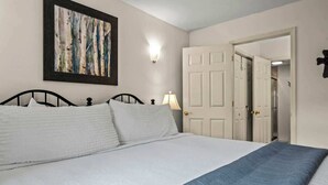 A bedroom with a bed, a painting, a wall-mounted light, and a door. - GC106•walk downtown•onsite pool•private hot tub (Gatlinburg)