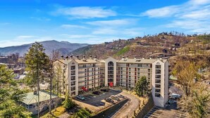 A multi-story hotel with a central courtyard, parking area, and a mountainous backdrop. - GC106•walk downtown•onsite pool•private hot tub (Gatlinburg)