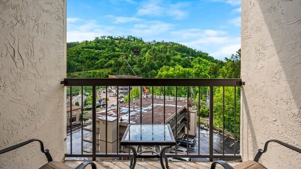 A balcony with a table and chairs, overlooking a parking area and buildings with a green hill in the background. - GC507•walk downtown •onsite heated pool (Gatlinburg)