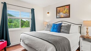 A bedroom with a bed, a window with curtains, a painting on the wall, and a nightstand with a lamp. - GC507•walk downtown •onsite heated pool (Gatlinburg)