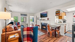 A modern living room with a fireplace, a dining area, and a kitchen with white cabinets and a TV mounted above the fireplace. - GC507•walk downtown •onsite heated pool (Gatlinburg)