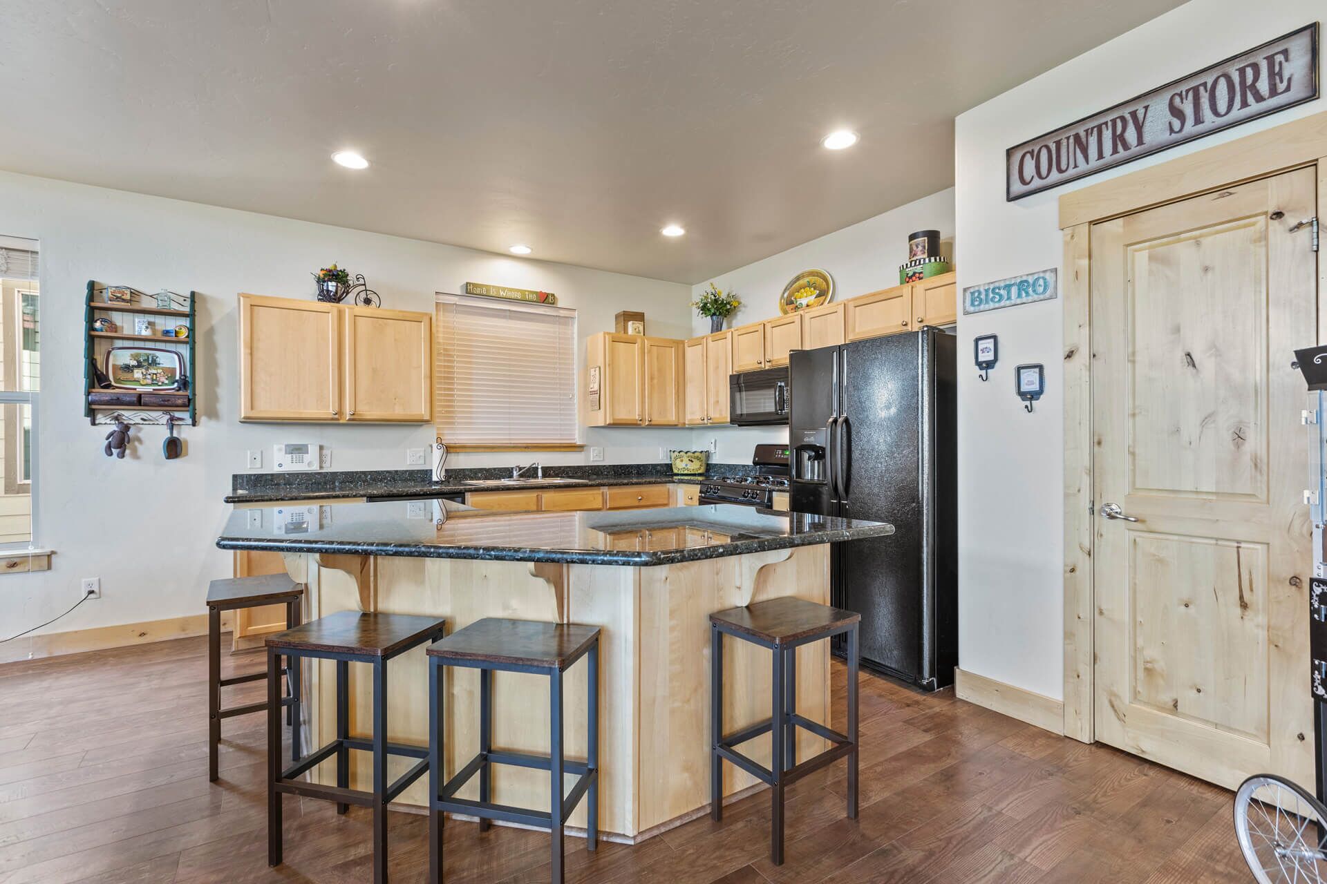 A kitchen with wooden cabinets, a black refrigerator, a coffee machine, and a sign that reads "COUNTRY STORE".