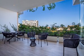 Un balcón con mobiliario exterior, barandilla de vidrio y vistas a edificios distantes.