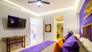 A bedroom with a bed, a TV, a wooden table, and a purple blanket. - Iconic Rooftop, Bar & Gym | Luxe 2 BR at Soho PV (Puerto Vallarta)